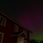 A red house with a green and purple aurora behind it